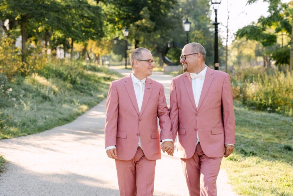 Twee bruidegoms in roze pakken lopen hand in hand door het park